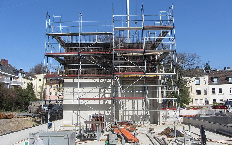 Rohbau eines mehrstöckigen Gebäudes mit Gerüst und Baustellenmaterialien bei sonnigem Wetter