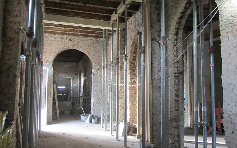 Sanierungsarbeiten in einem Altbau mit Rundbögen, freigelegtem Mauerwerk und Stahlstützen zur Abfangung der Decke