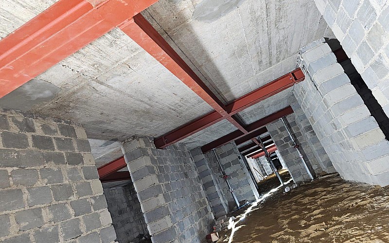 Kellerrohbau mit roter Stahlträgerkonstruktion und unverputztem Mauerwerk, Boden noch unbefestigt